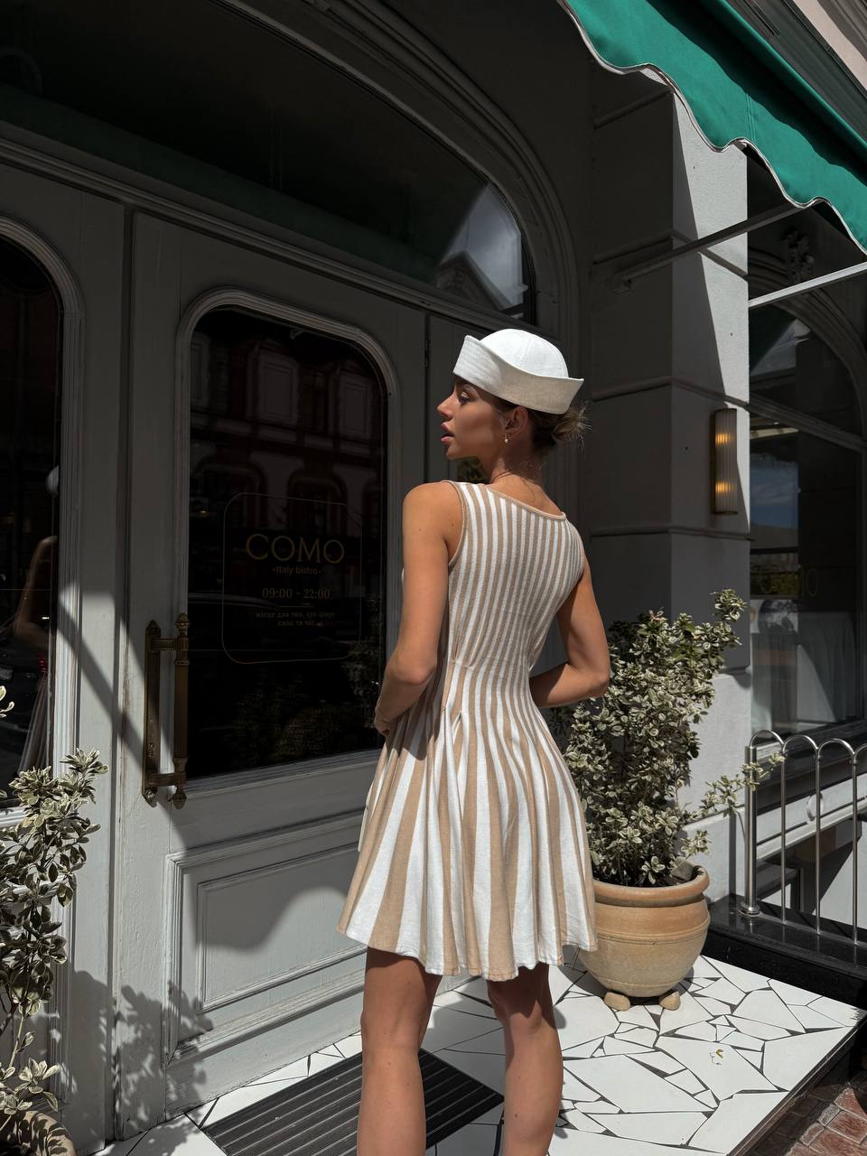 Woman in a striped dress standing outside a building with a green awning.