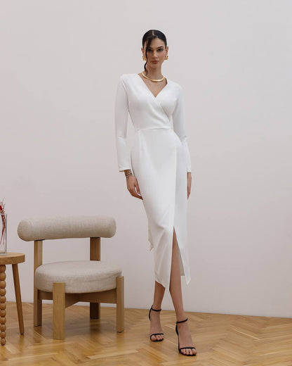 Woman in a white dress standing in a room with a chair and table.