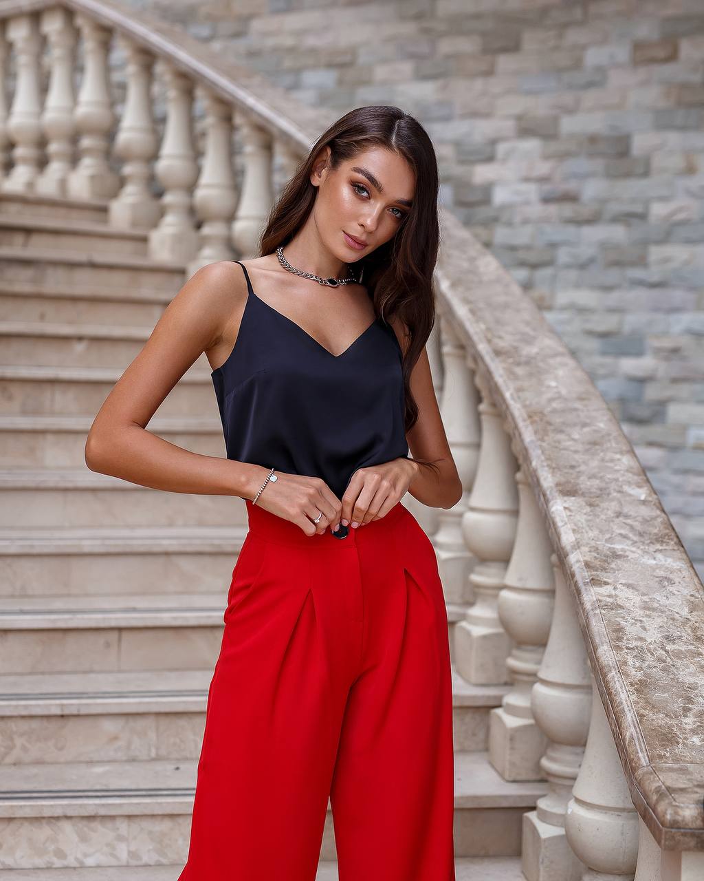 Woman in black top and red pants standing on stone steps with stone wall background