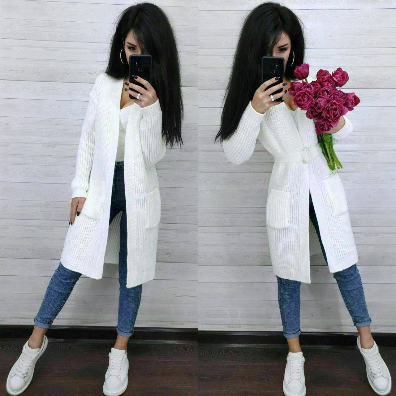 Woman in a white coat taking a mirror selfie with a bouquet of flowers.
