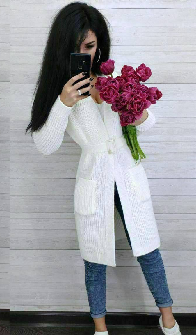 Person wearing a white cardigan holding pink flowers against a light background