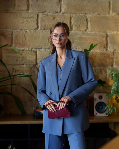 Woman in a blue suit holding a purple clutch against a brick wall.
