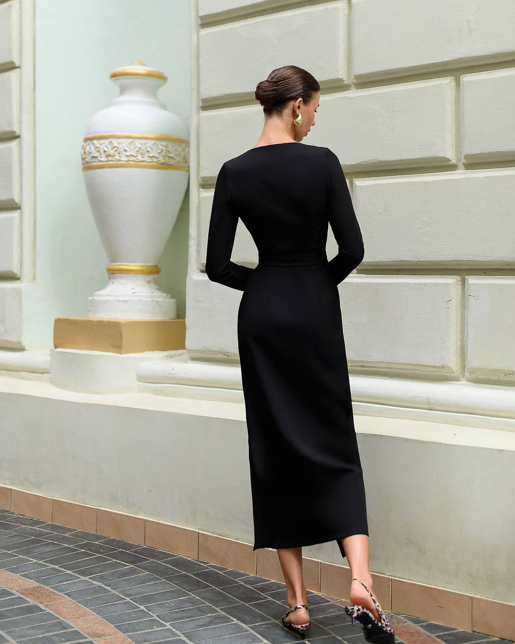 Woman in a black dress walking away from the camera in an elegant interior setting.