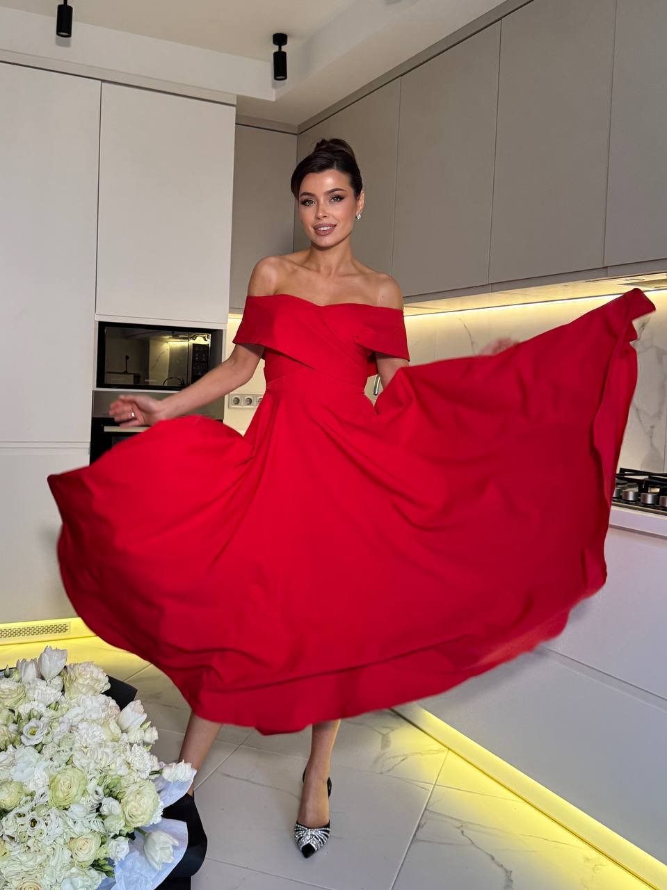 Woman in a red off-shoulder dress posing in a modern kitchen.
