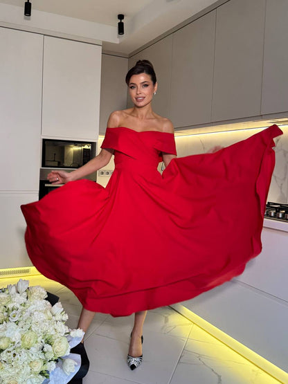 Woman in a red off-shoulder dress posing in a modern kitchen.