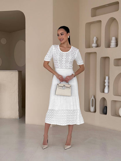Woman in a white lace dress standing in a modern interior setting.