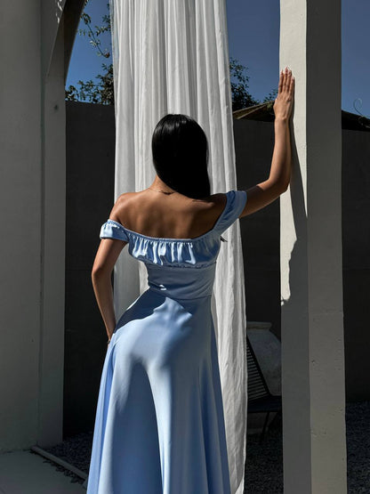 Woman in a blue dress standing behind white curtains