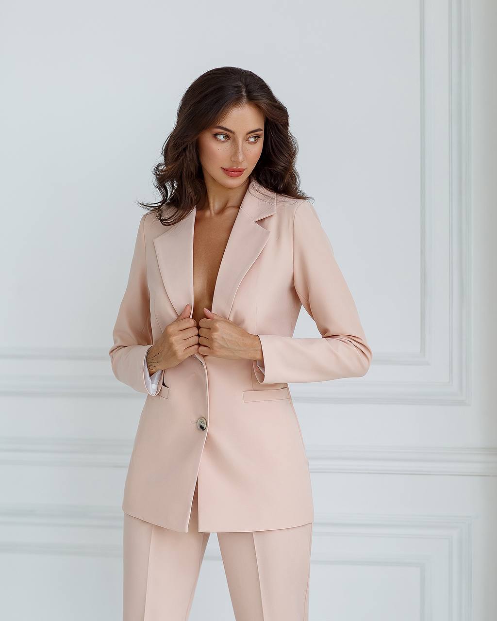 Woman wearing a light pink suit against a white wall