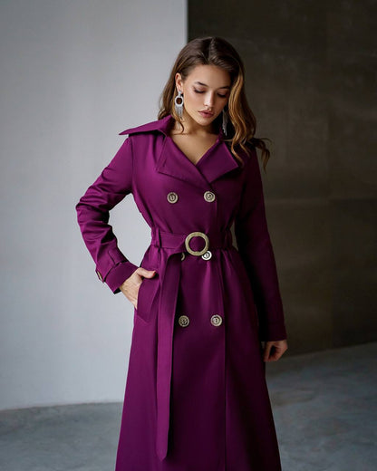 Woman wearing a purple trench coat with gold buttons against a neutral background