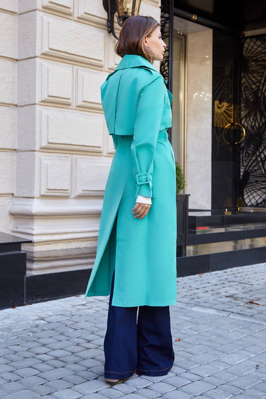 Woman wearing a turquoise coat standing on a street with a building in the background