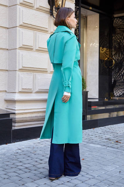 Woman wearing a turquoise coat standing on a street with a building in the background