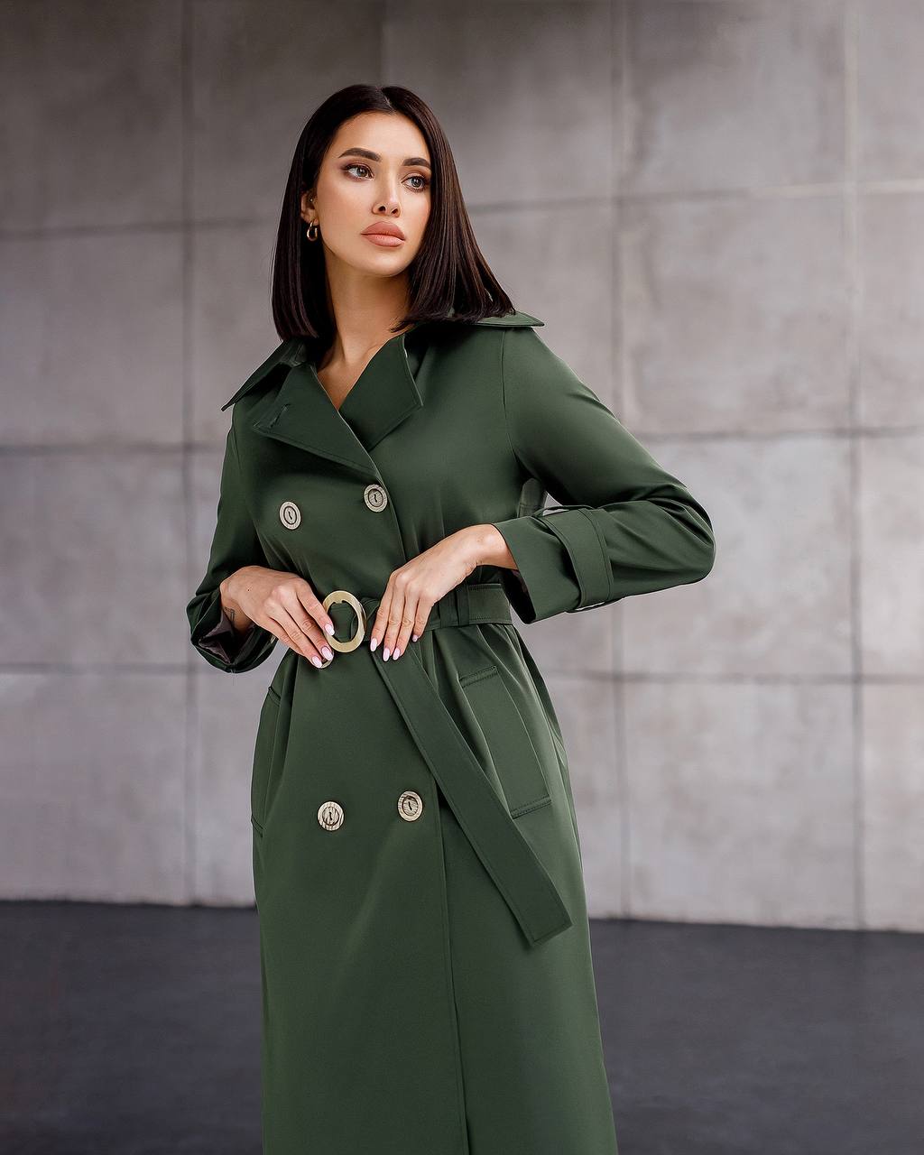 Woman wearing a green trench coat against a gray background