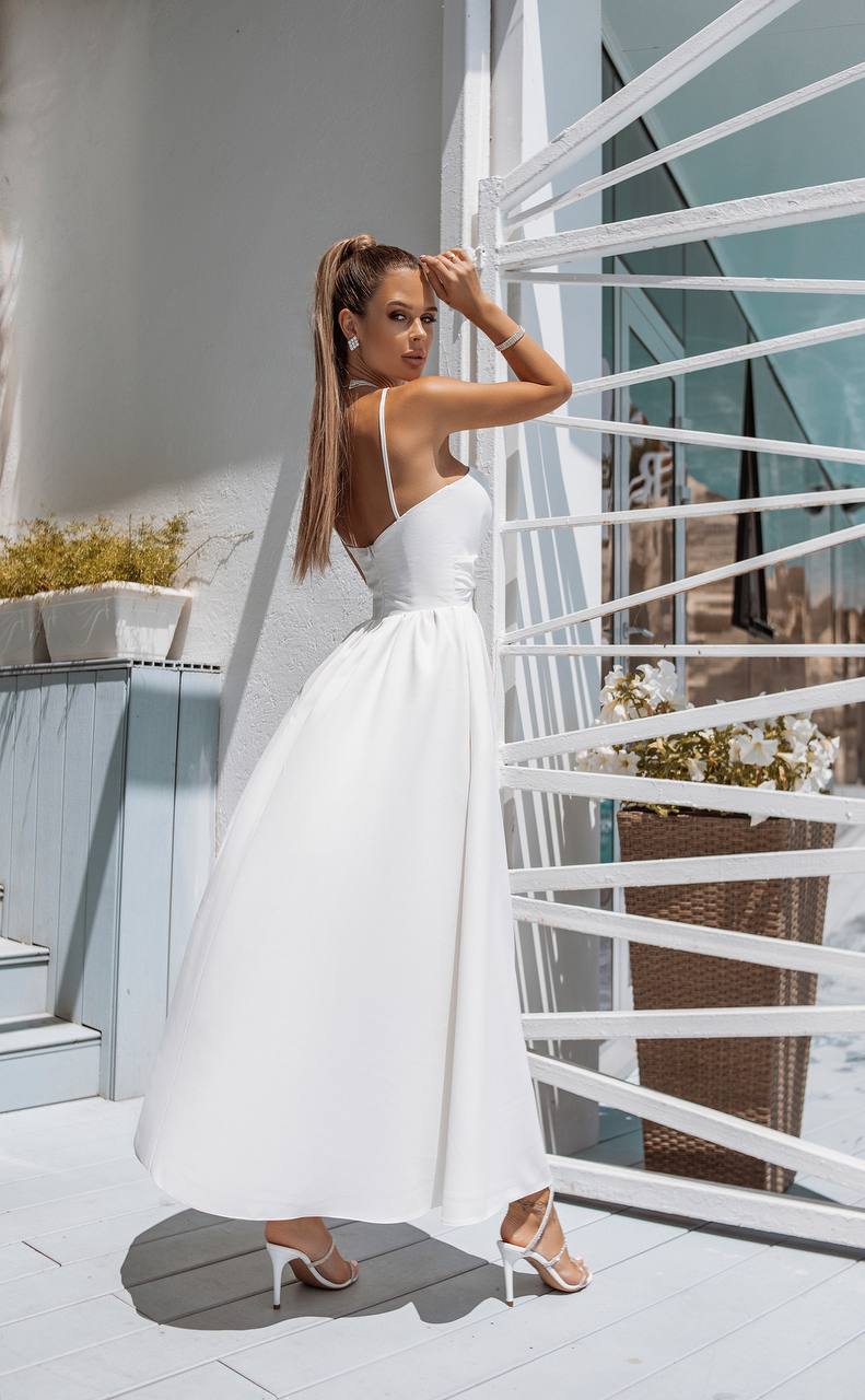 Woman in a white dress standing on a balcony with a modern architectural background