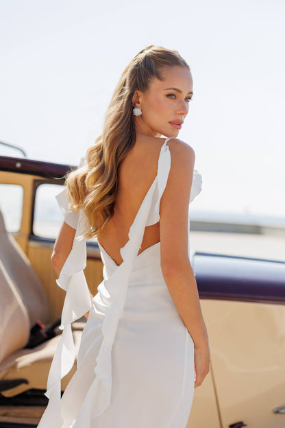 Woman in a white wedding dress standing next to a vintage car.