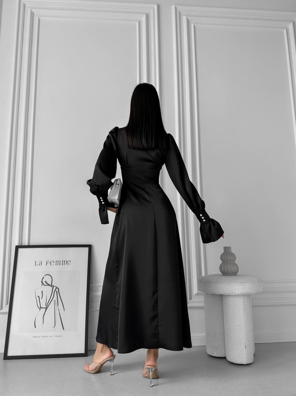 Woman in a black dress standing in a room with white walls and decor.