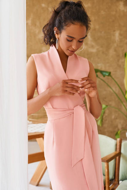 Woman in a pink dress standing indoors with a neutral background