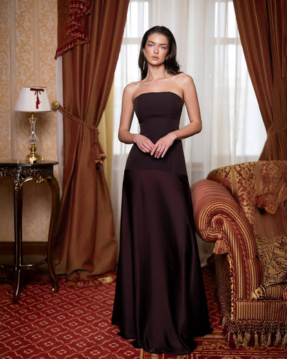 Woman in a strapless brown evening gown standing in an elegant room with red carpet and ornate furniture.