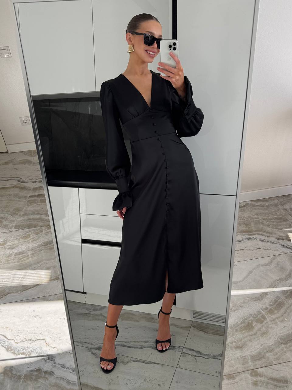 Woman taking a mirror selfie wearing a black dress in a modern interior setting.
