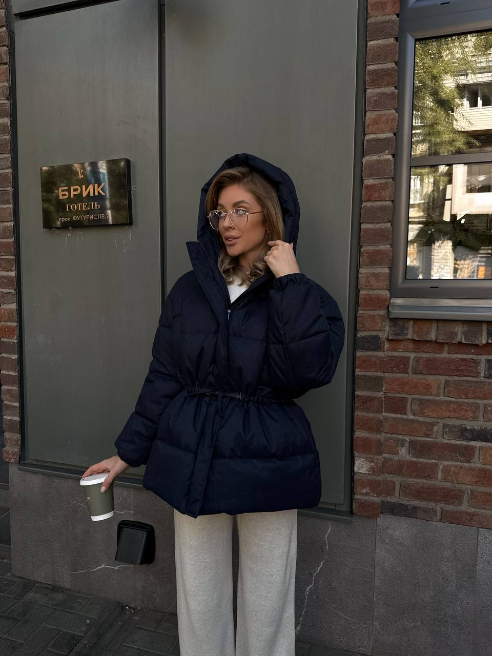 Person wearing a dark blue puffer jacket standing outside a building with a sign.