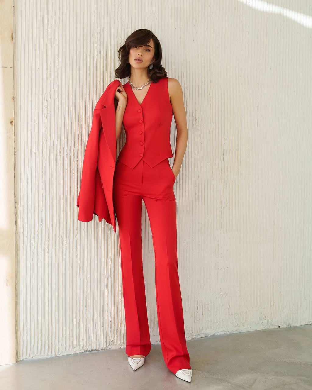 Woman wearing a red suit standing against a light-colored wall.