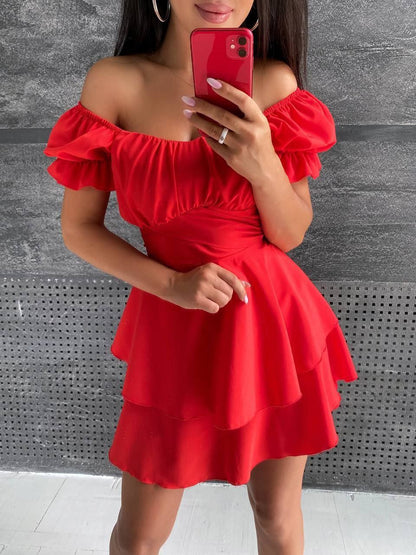 Woman wearing a red off-shoulder dress against a gray wall.