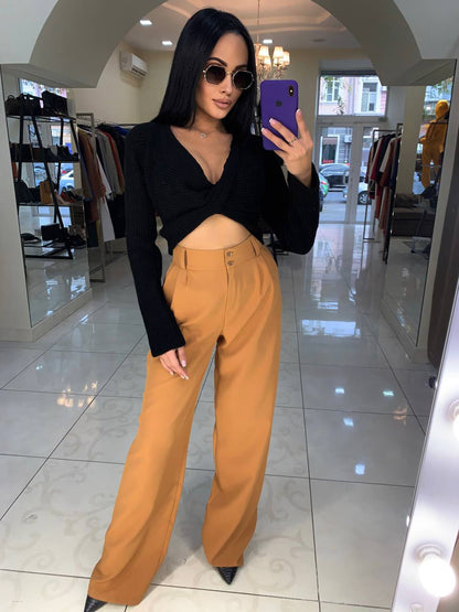 Woman taking a mirror selfie wearing a black top and mustard yellow pants in a store.