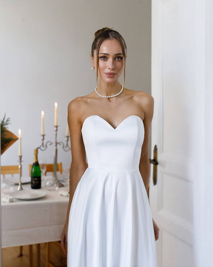 Woman in a white strapless dress standing in a room with a dining table and candles.