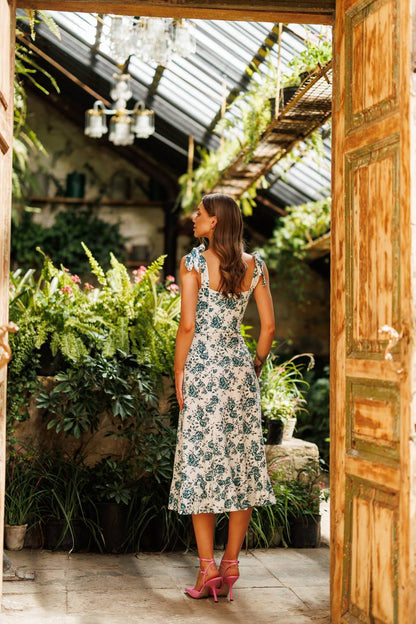 Woman in a floral dress standing in a garden with a wooden door open