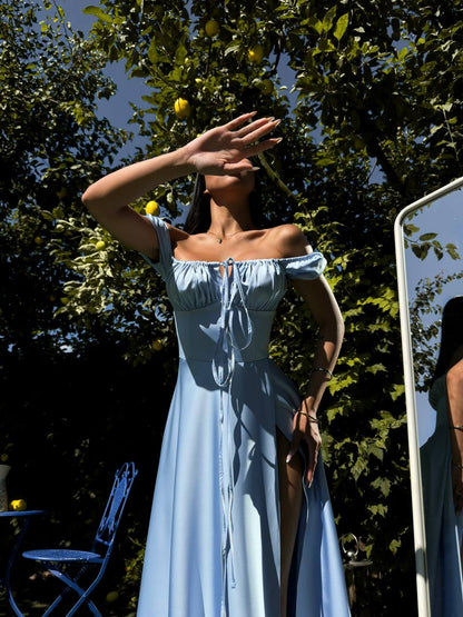 Woman in a light blue dress standing outdoors with trees and a chair in the background