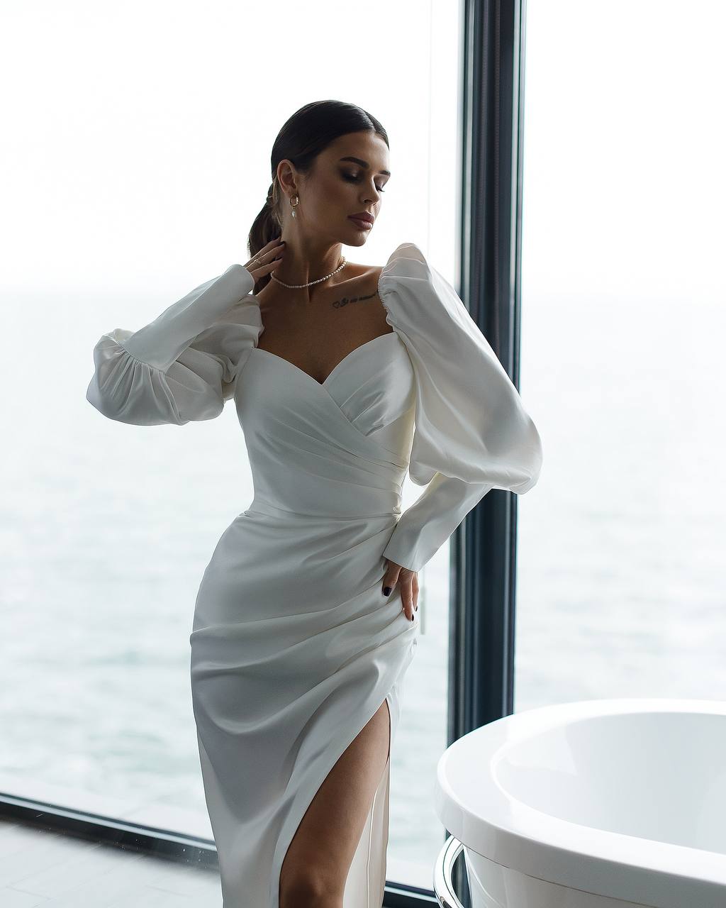 Woman wearing a white dress with long sleeves in a modern interior setting.