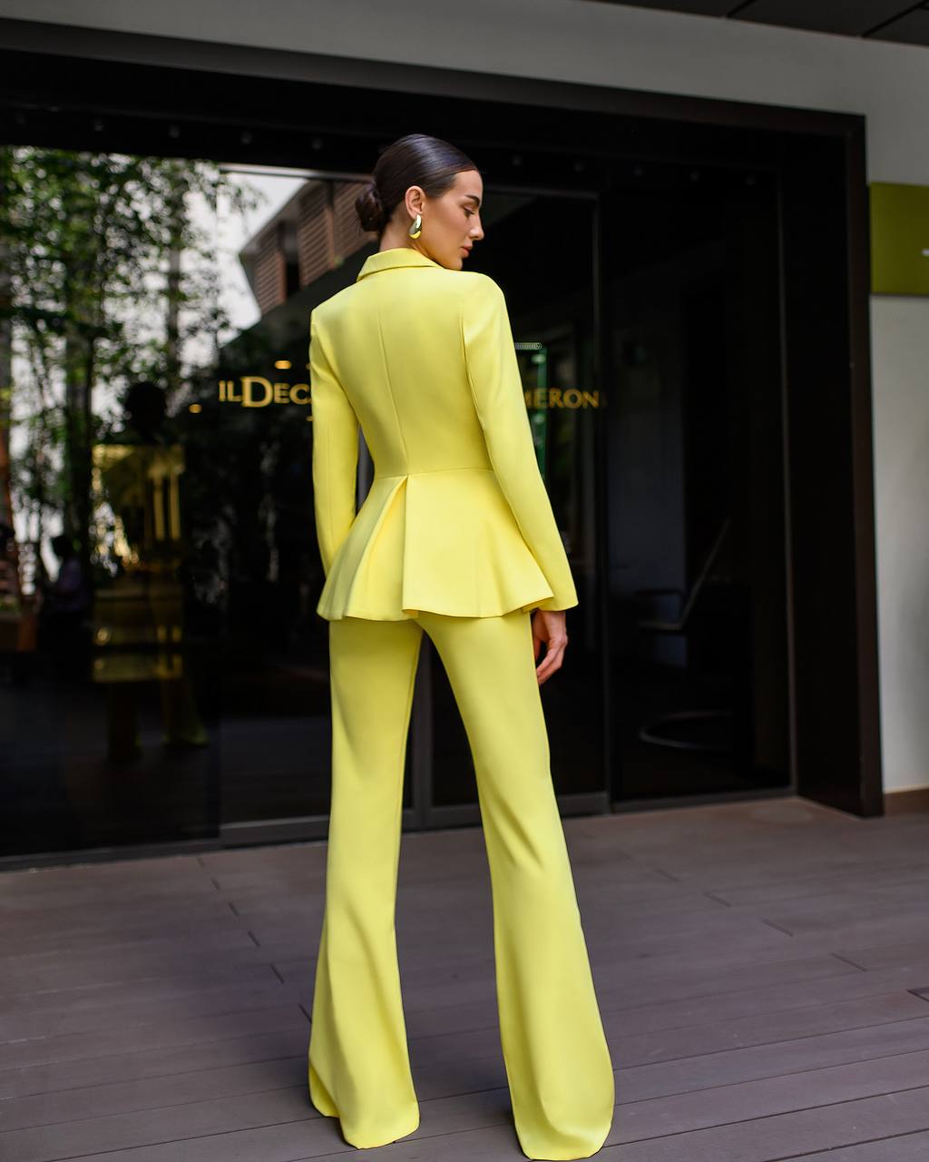 Woman in a bright yellow suit standing in front of a store entrance.