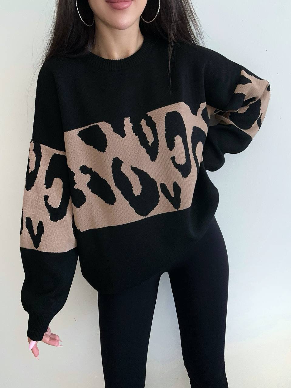 Person wearing a black sweater with beige leopard print sleeves against a white background