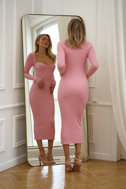 Woman in a pink dress standing in front of a mirror in a room with white walls and wooden floor.