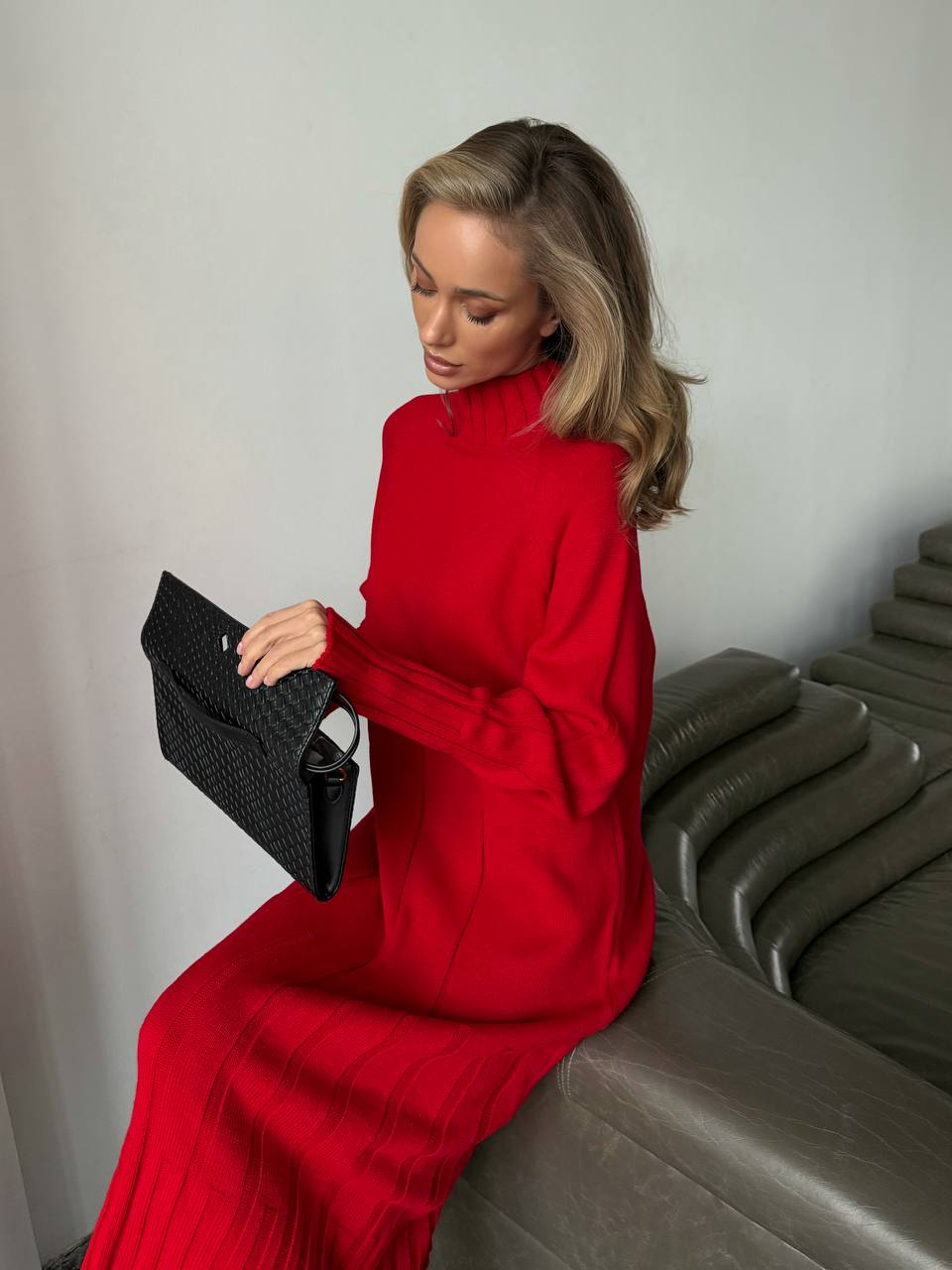 Woman in a red dress holding a black clutch against a neutral background