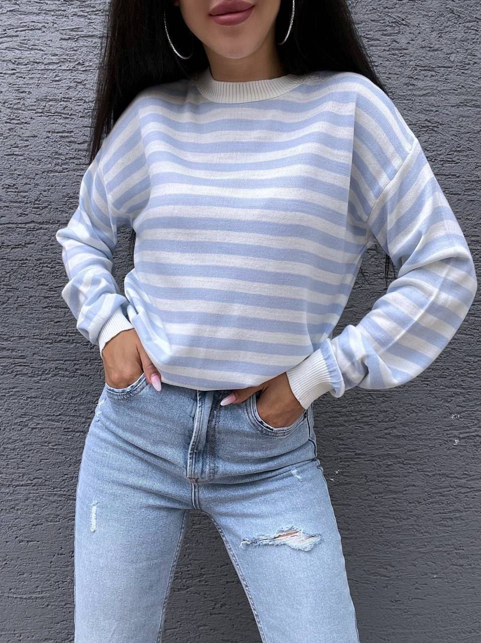 Person wearing a blue and white striped sweater and light blue jeans against a gray background