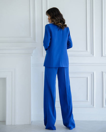 Person wearing a blue suit standing against a white paneled wall.