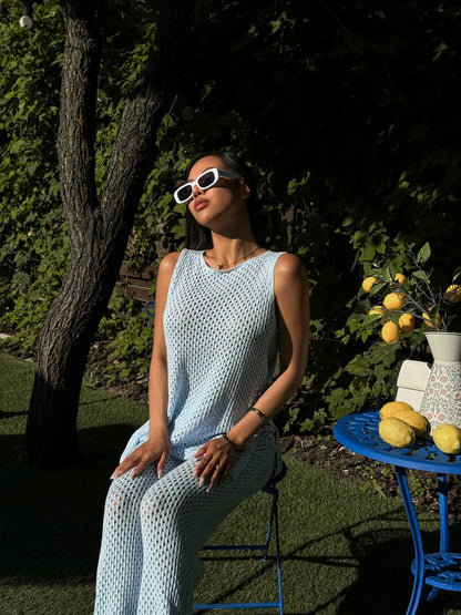 Woman in a light blue sleeveless top and pants sitting outdoors with sunglasses on, near a table with lemons.