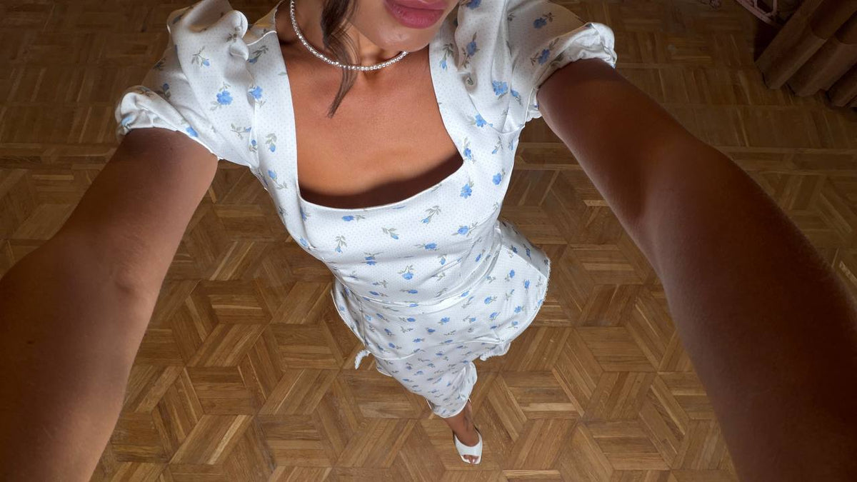 Person wearing a white dress with blue patterns on a wooden floor.