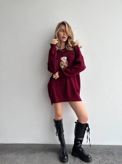 Woman wearing a burgundy sweater dress with black knee-high boots against a plain background