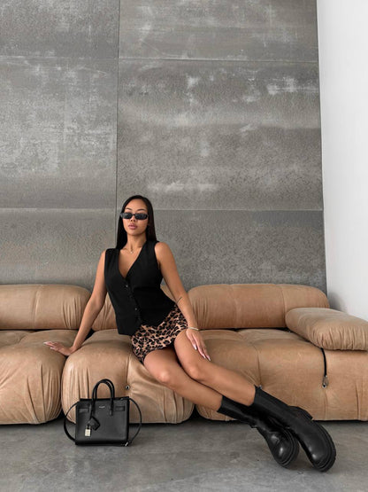 Woman sitting on a beige sofa with a black handbag in front of a gray wall.