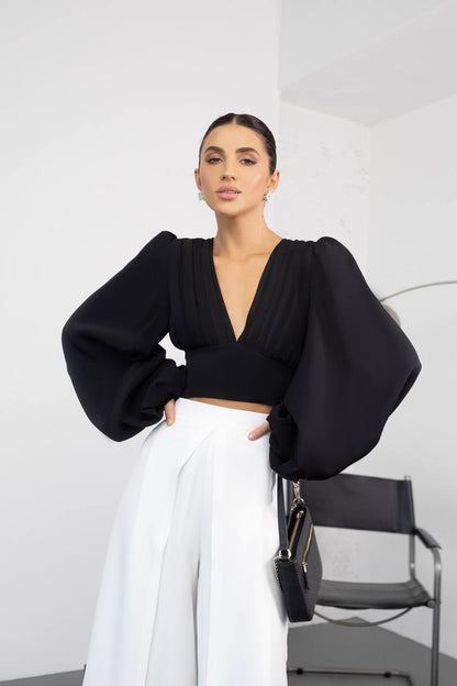Woman wearing a black top and white pants in a minimalistic setting