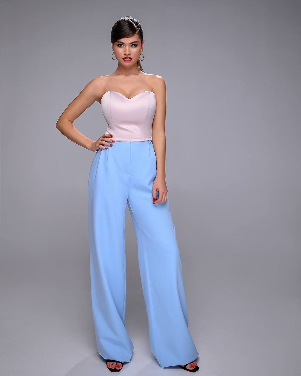 Woman wearing a strapless pink top and light blue pants on a gray background