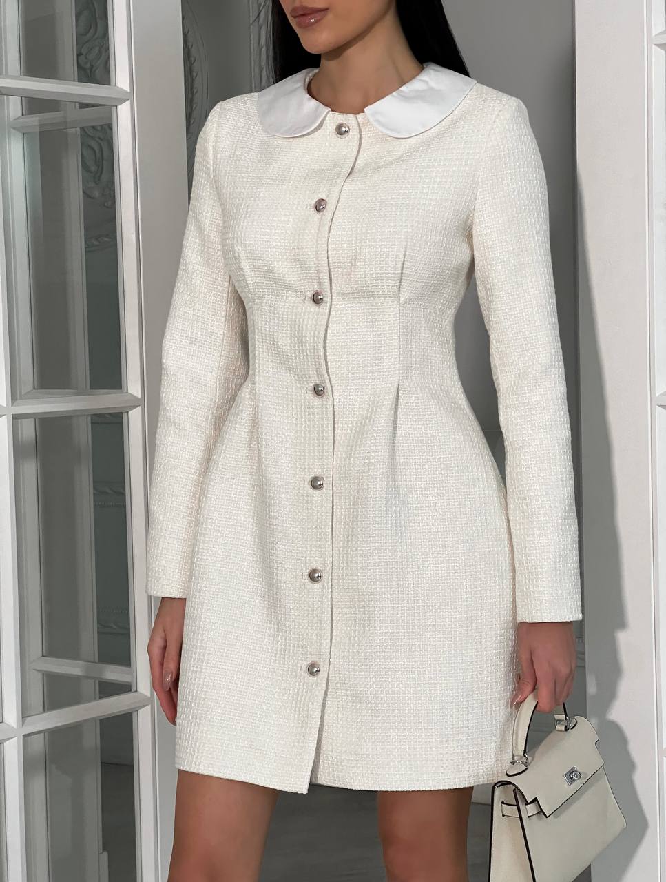 Woman wearing a white dress with a Peter Pan collar against a neutral background