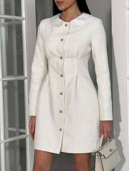 Woman wearing a white dress with a Peter Pan collar against a neutral background