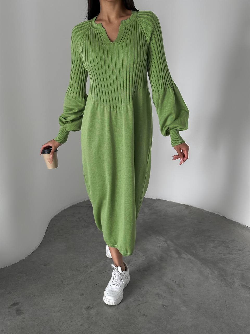 Person wearing a green ribbed dress with white sneakers on a gray background