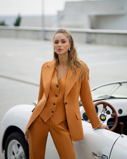 Woman in a mustard yellow suit standing next to a vintage car.