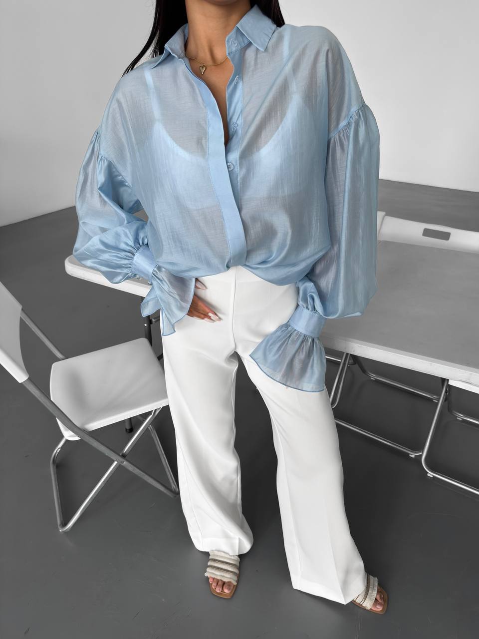 Person wearing a light blue sheer blouse and white pants sitting on a chair.