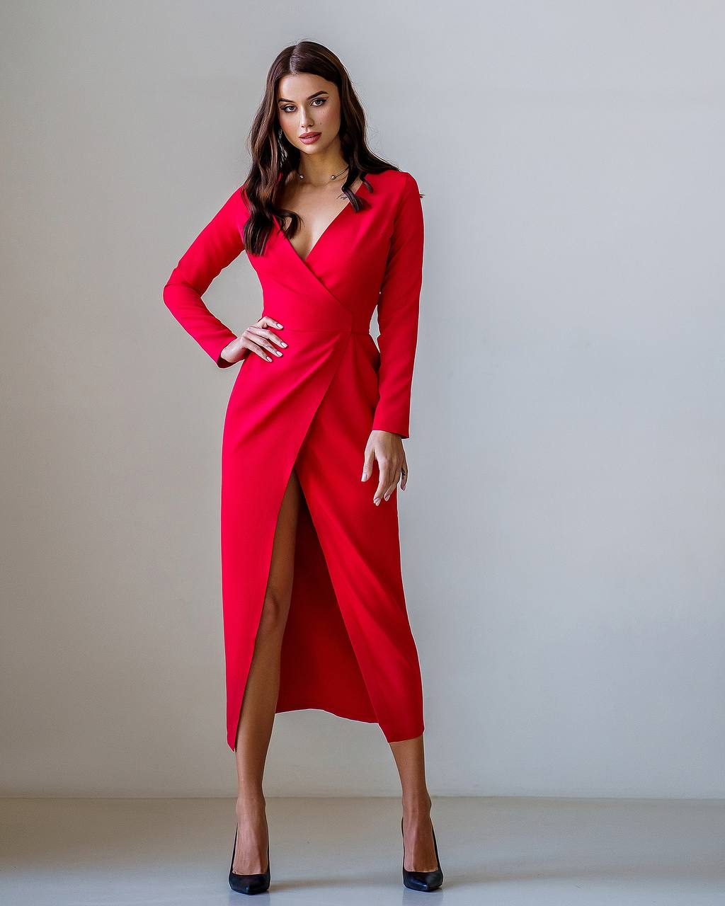 Woman wearing a red dress with a high slit on a plain background