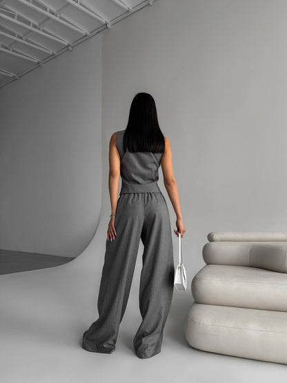 Woman in a gray jumpsuit standing in a minimalistic room with a modern sofa.