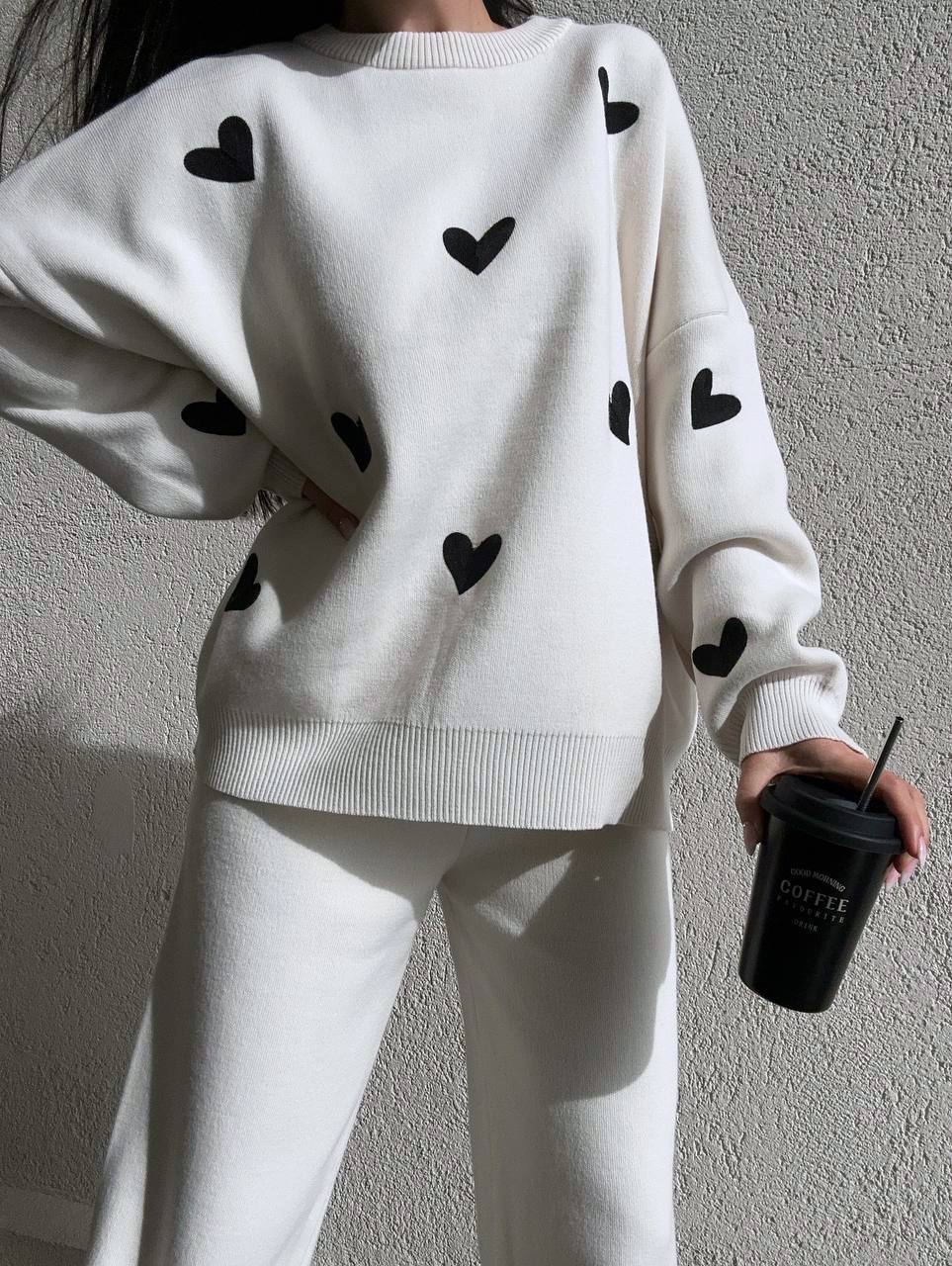 White sweater with black heart patterns worn by a person against a plain background